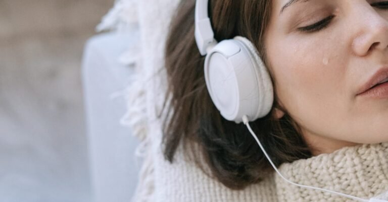 Young woman lying down indoors, wearing headphones and a knitted sweater, with tears on her face.